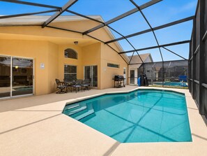 Une piscine intérieure avec un patio couvert, un barbecue et un espace aménagé pour s’asseoir.