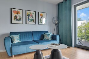 A modern living room with a blue sofa, two white round tables, and three abstract paintings on the wall. - Nadmorze Seaside Apartment with Parking  (Gdańsk)