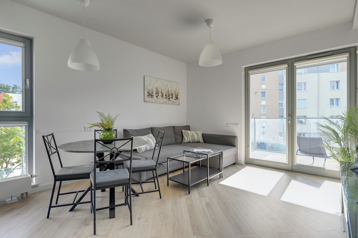 A modern living room with a sofa, a dining table with chairs, and a coffee table. There is a painting on the wall and a window with a view of buildings.