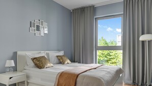 Quarto moderno com uma grande janela, uma cama com cobertura acolchoada e uma mesa de cabeceira com abajur.
