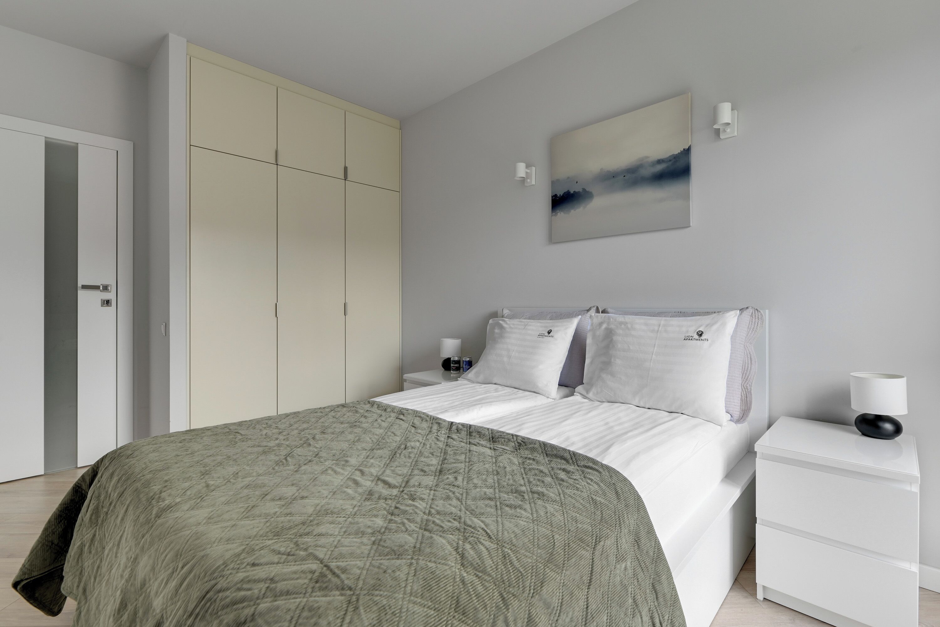 A bedroom with a bed, a wardrobe, a nightstand, a lamp, and a painting on the wall.