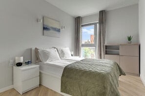 A bedroom with a bed, a nightstand, a window with curtains, a painting, and a small plant on a shelf. - Nadmorze Seaside Apartment with Parking  (Gdańsk)