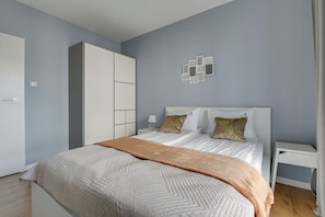 A bedroom with a bed, nightstands, a wardrobe, and a wall with geometric patterns. - Nadmorze Seaside Apartment with Parking  (Gdańsk)