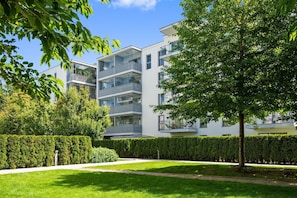A modern multi-story residential building with balconies, surrounded by well-maintained hedges and a grassy lawn. - Nadmorze Seaside Apartment with Parking  (Gdańsk)