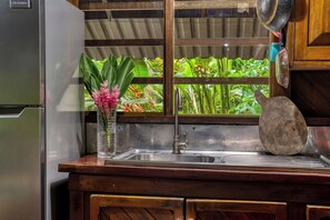 A kitchen with a stainless steel sink, a wooden countertop, and a window with a view of greenery.