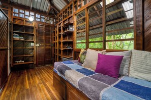 A cozy room with a wooden floor, a bed with a quilt, and a large window with a view of greenery.