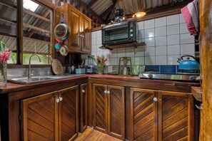 A kitchen with wooden cabinets, a microwave, a kettle, and various kitchen utensils. - Wooden Cabin with Yoga deck over Creek, Walk to the Beach (Puntarenas Province)