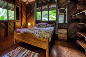 A wooden bedroom with a bed, a nightstand, a dresser, and a window with a view of greenery.