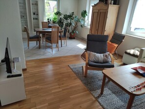 Olohuone, jossa on ruokailutila, puulattia, suuri ruukussa oleva kasvi, kaappi ja televisio.