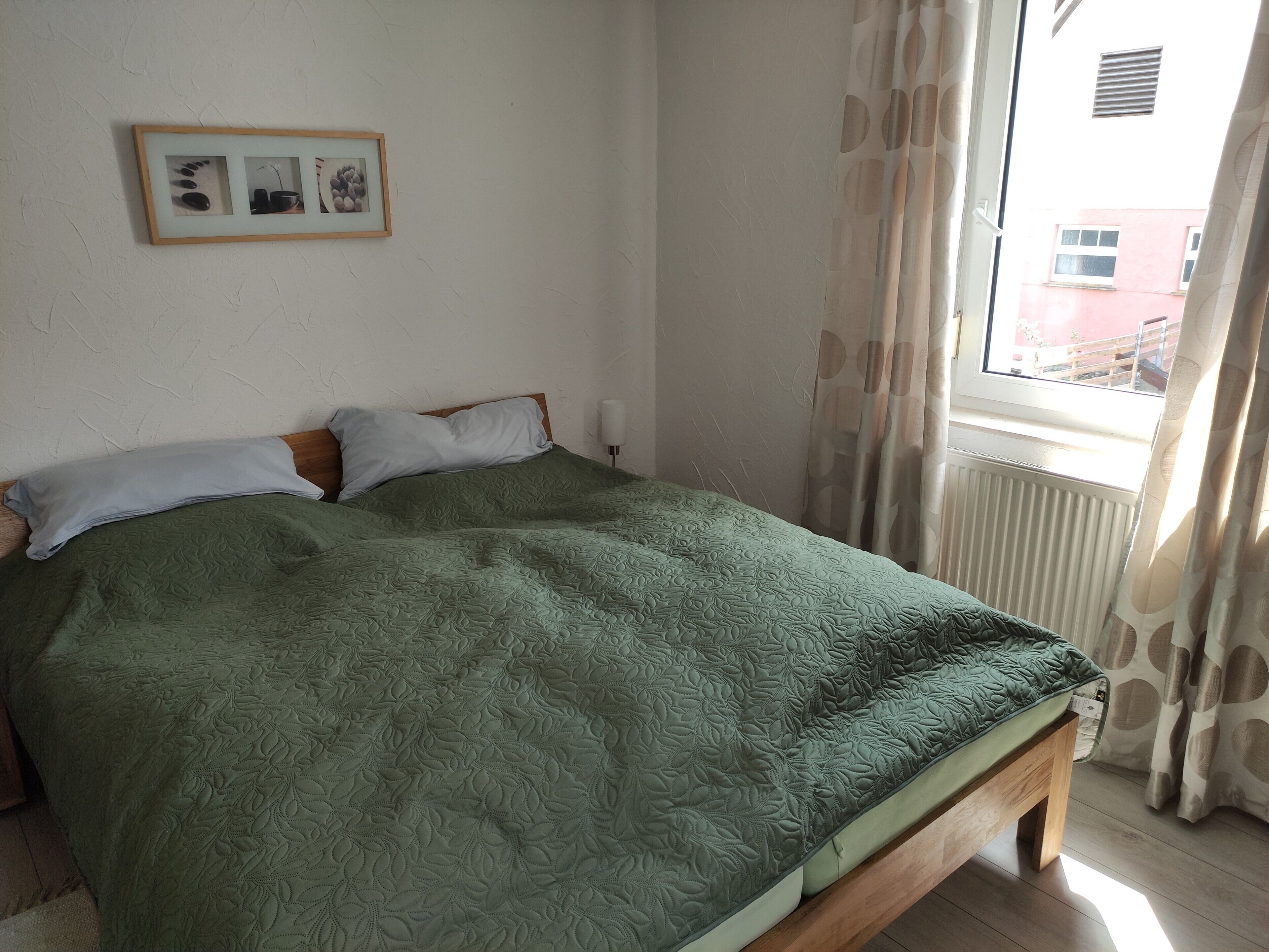 Ein Zimmer mit einem Bett, einem gerahmten Bild an der Wand und einem Fenster mit Vorhängen.