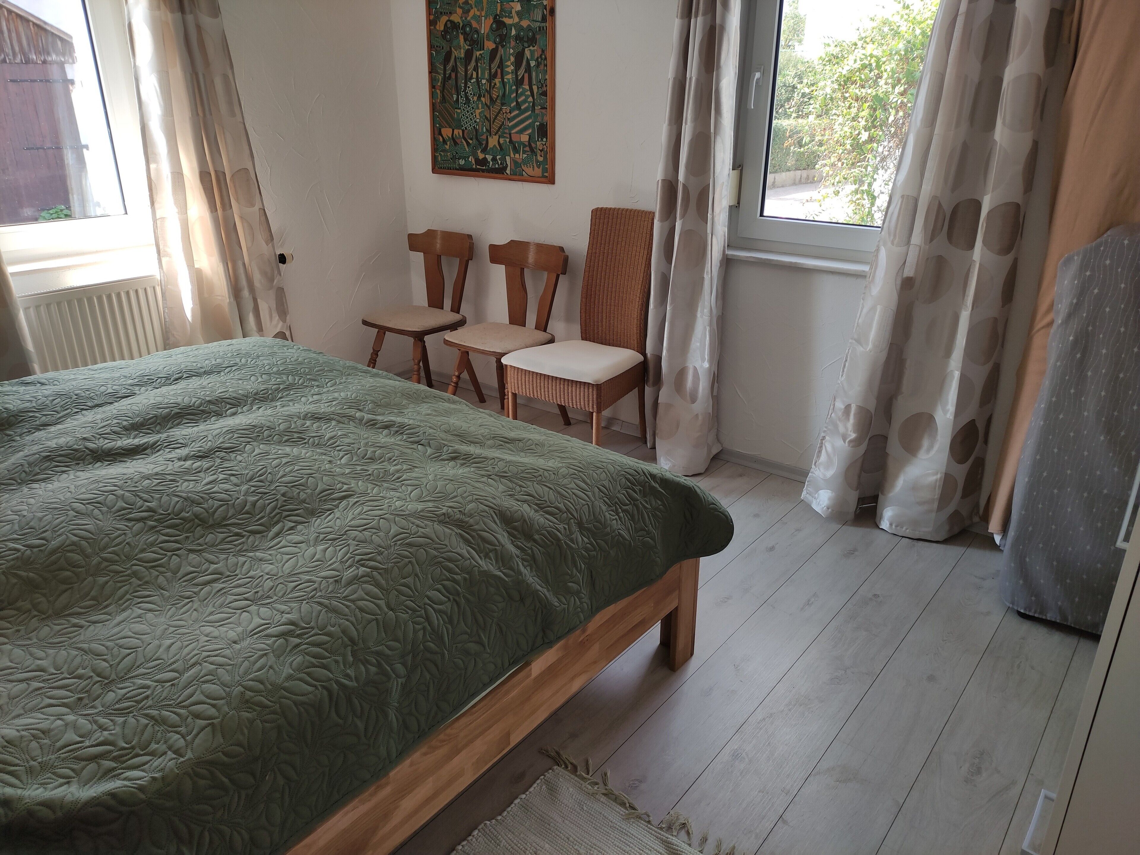 Une pièce avec un lit, deux chaises, une fenêtre et un tableau au mur.