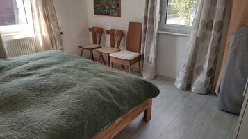 Une pièce avec un lit, deux chaises, une fenêtre et un tableau au mur.