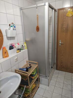 Kylpyhuone, jossa on suihku, puuovi, pesuallas ja hylly, jossa on hygieniatuotteita.