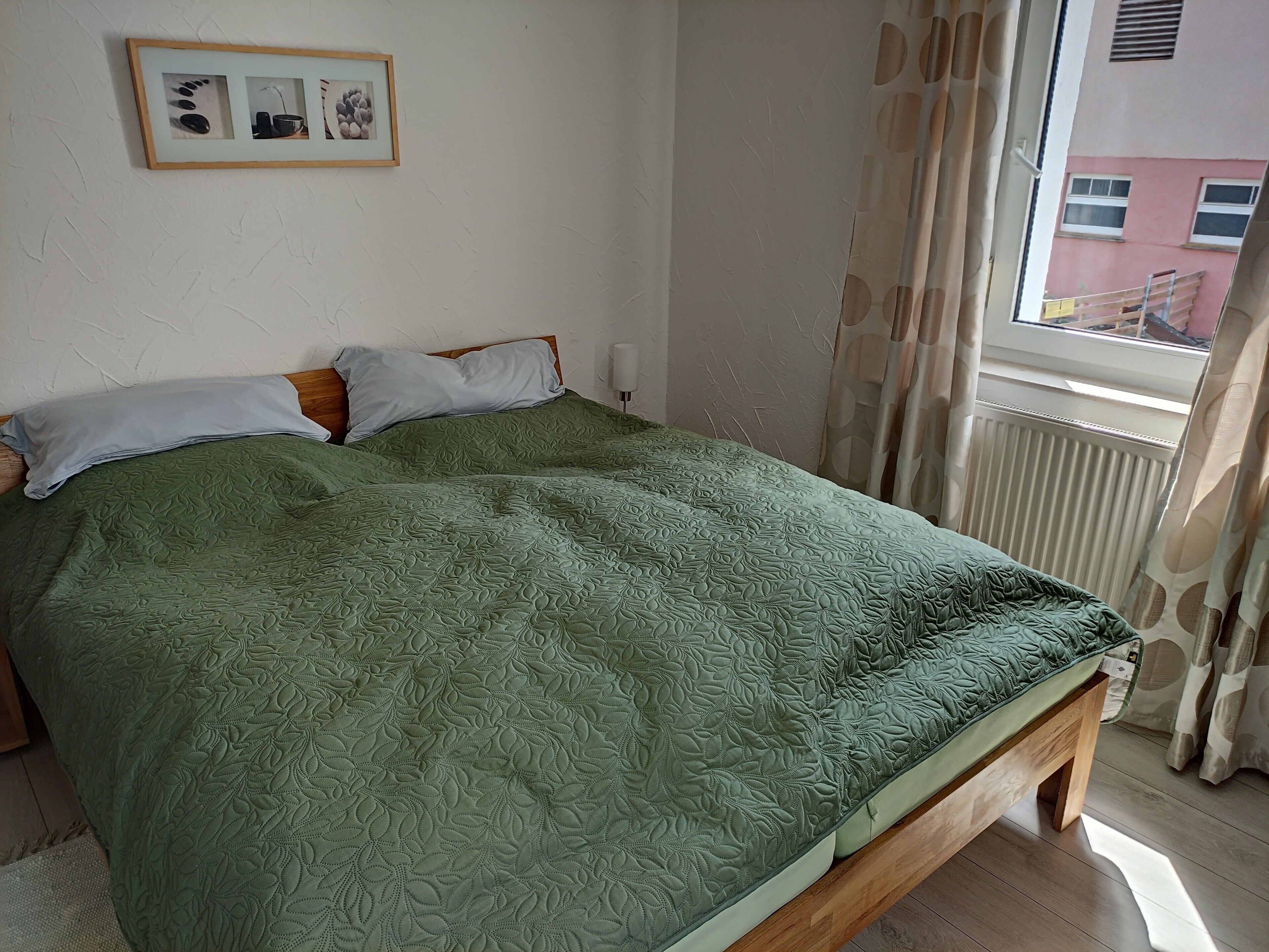 Un letto con una coperta verde, una testiera in legno e una finestra con tende.