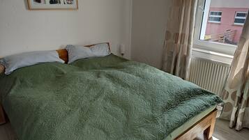 Un letto con una coperta verde, una testiera in legno e una finestra con tende.