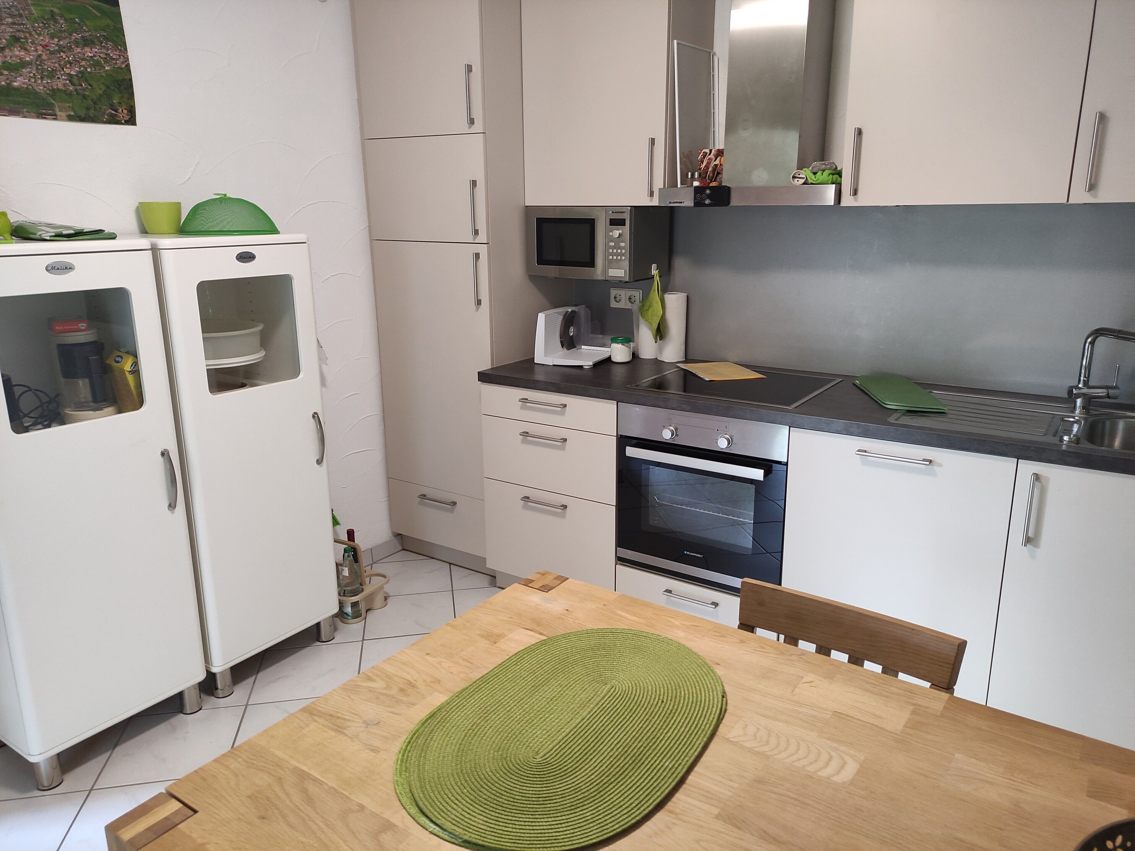 Una cucina compatta con mobili bianchi, un forno a microonde, un forno e un lavandino.