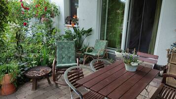 Une terrasse avec une table et des chaises en bois, entourée de plantes en pot et d’une variété de verdure.