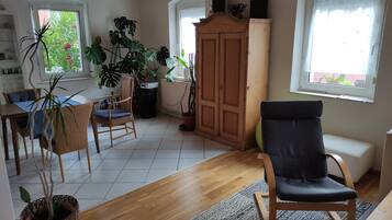 Un vaste espace de vie doté d’un plancher en bois, d’une table à manger avec des chaises, d’un fauteuil noir rembourré et de plusieurs plantes en pot.