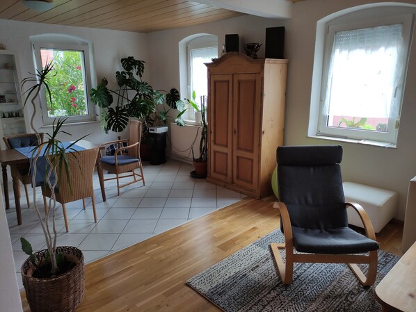 Tilava olohuone, jossa on puulattia, ruokapöytä tuoleineen, musta pehmustettu tuoli ja useita ruukkukasveja.