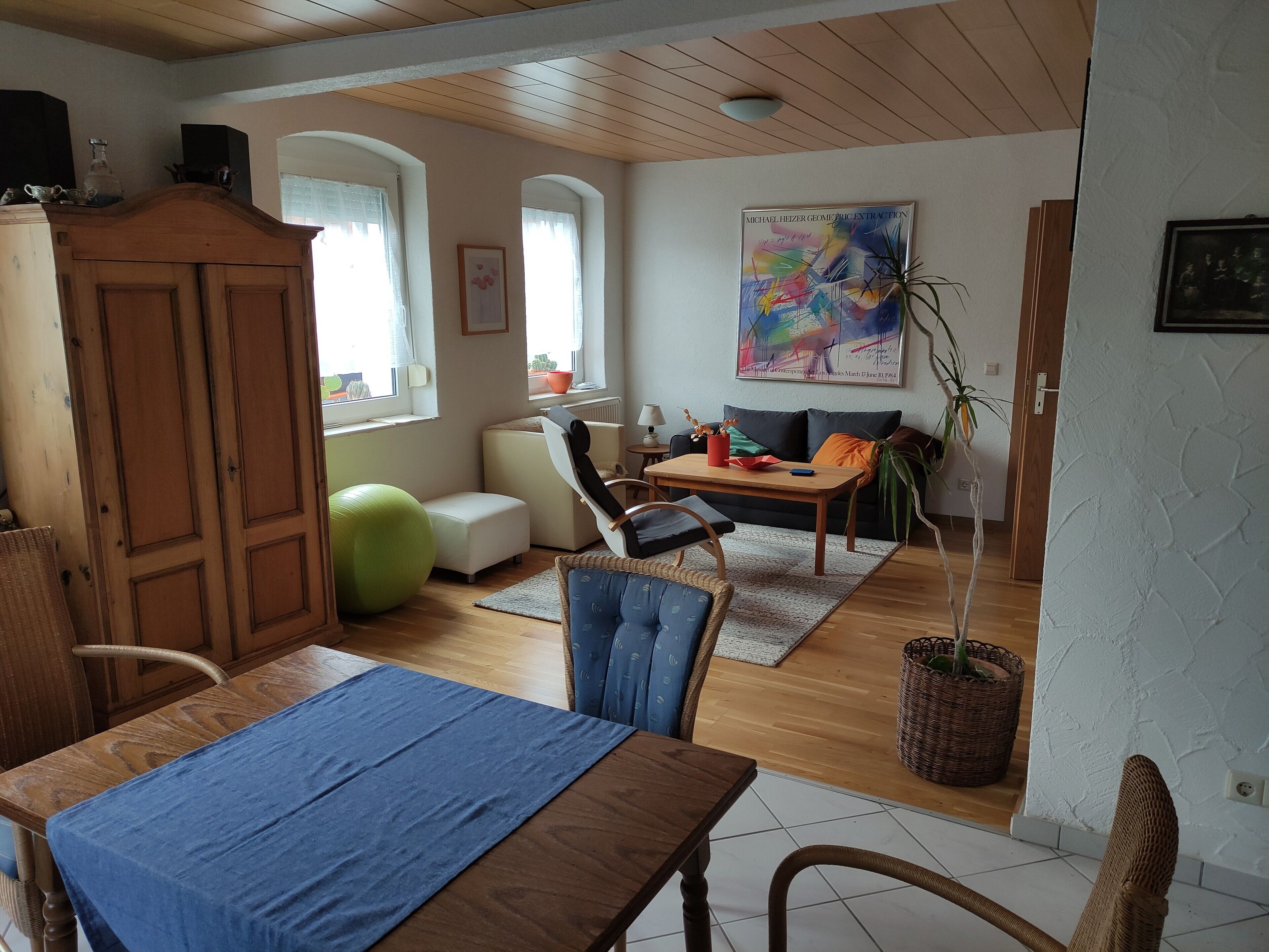 A living room with a dining area, wooden furniture, a green exercise ball, a sofa, and a painting on the wall.