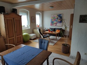Una sala de estar con comedor, muebles de madera, una pelota de ejercicio verde, un sofá y un cuadro en la pared.