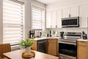 Une cuisine moderne avec des meubles blancs, des appareils en acier inoxydable et un coin repas comprenant une table en bois et une plante en pot.