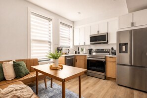 Une cuisine moderne avec des meubles blancs, des appareils en acier inoxydable et une table à manger en bois.
