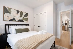 Een hotelkamer met een bed, een nachtkastje, een schilderij, een deur en uitzicht op de keuken.