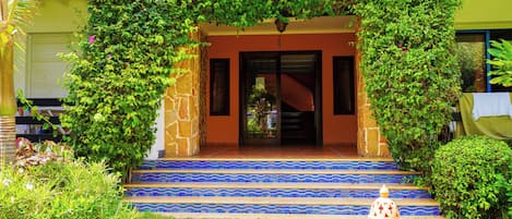 Una entrada de edificio con una escalera de piedra, una puerta y un pequeño jardín con un hidrante.