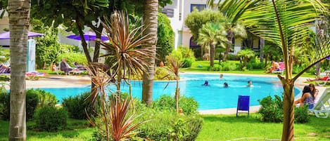 A pool area with lounge chairs, palm trees, and a clear blue pool.