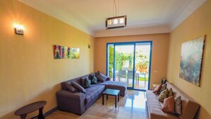 A living room with a sectional sofa, a small table, and a painting on the wall. - Green Haven in Skhirat, Pool & Walk to the Beach (Skhirat)