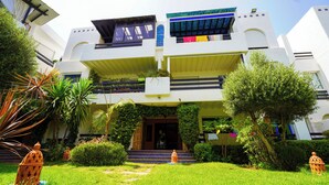 A two-story building with a flat roof, balconies, and a small garden area with a pathway leading to the entrance. - Green Haven in Skhirat, Pool & Walk to the Beach (Skhirat)