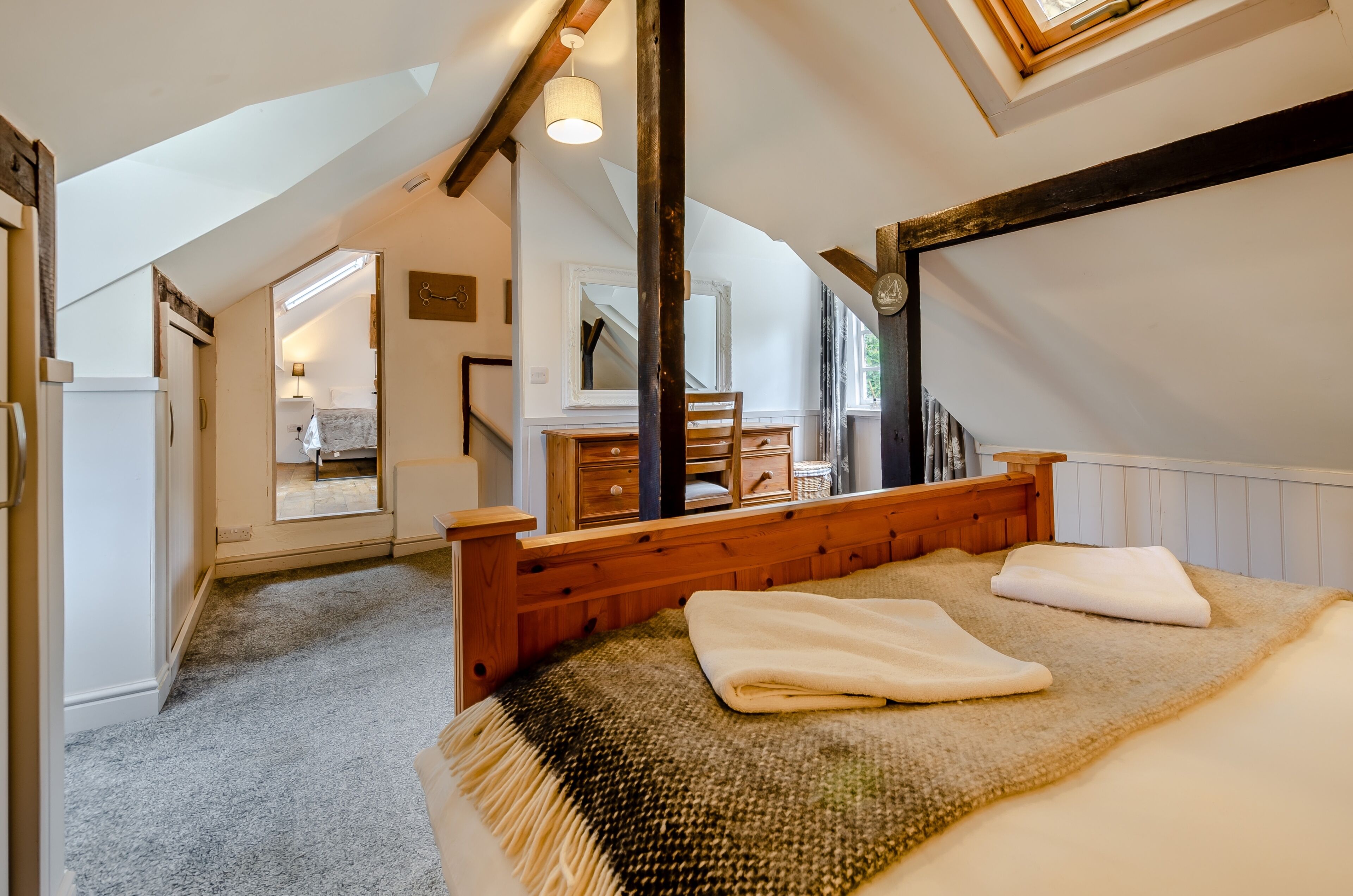 A bedroom with a wooden bed, a mirror, a dresser, and a view of a hallway.