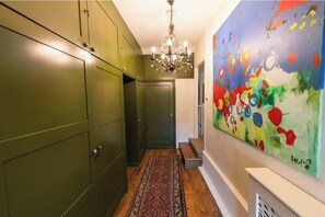 A hallway with green cabinets, a chandelier, a patterned rug, and a colorful abstract painting. - Historic Log Farmhouse on Flying Cloud Farm (Fairview)