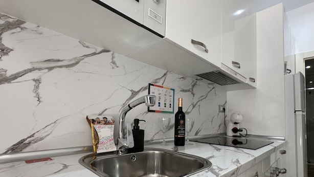 Cozinha moderna com bancada de mármore, pia de aço inoxidável e uma garrafa de vinho.