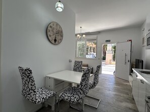 Een eethoek met een witte tafel en gestreepte stoelen, een wandklok, en uitzicht op het omliggende landschap.