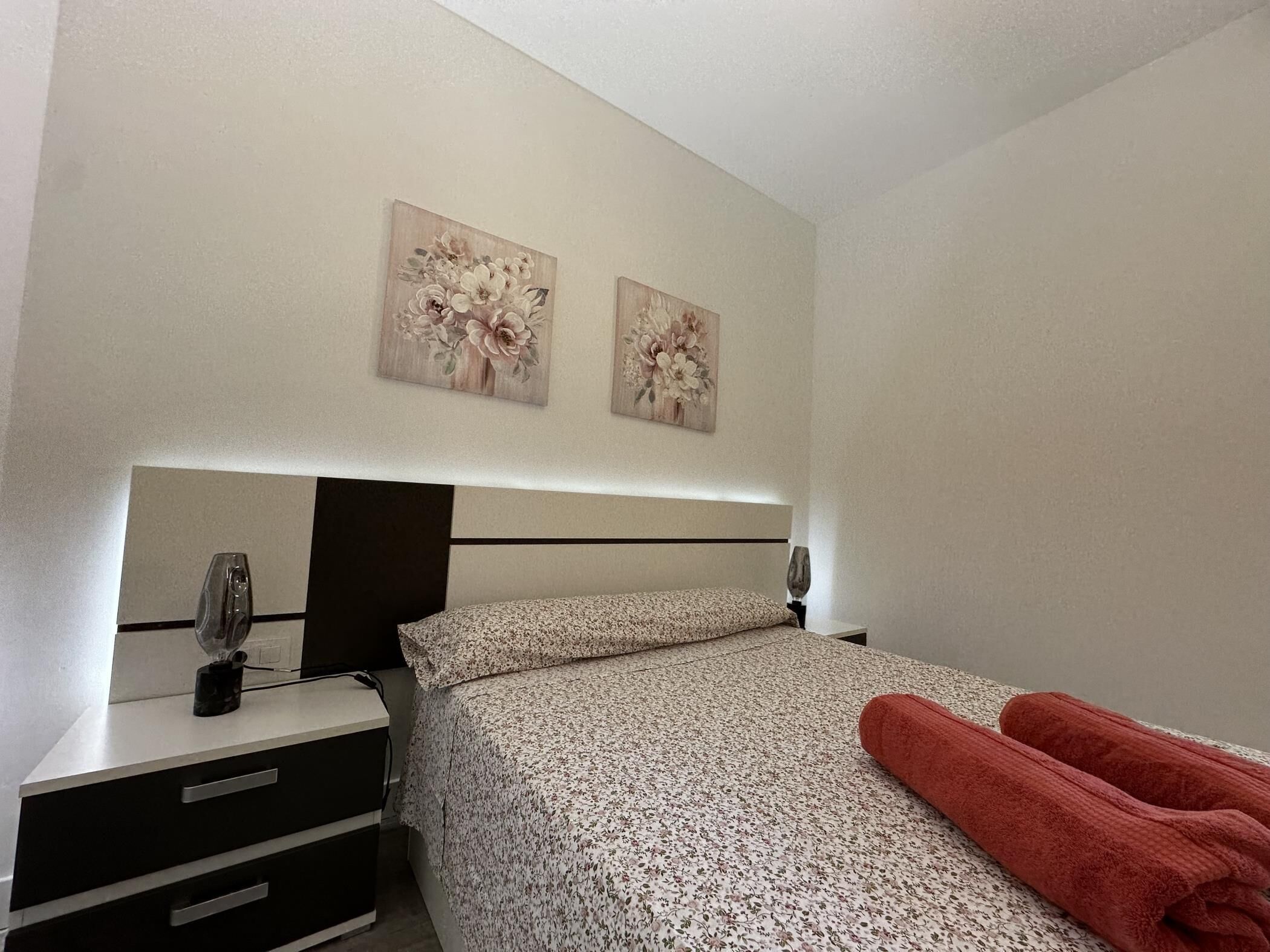 Ein Hotelzimmer mit einem Bett, einem Nachttisch, einer Lampe und zwei an der Wand hängenden Bildern.