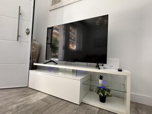 A modern entertainment unit with a flat-screen TV, a white console, and a glass shelf with a potted plant. - 2-Bedroom Apartment with Parking, 100 m from La Carihuela Beach (Torremolinos)
