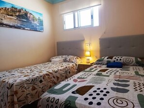 Een kamer met twee bedden, een raam, een schilderij aan de muur en een bedlampje.