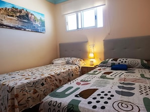 Ein Schlafzimmer mit zwei Betten, einem Fenster, einem Bild an der Wand und einer Nachttischlampe.