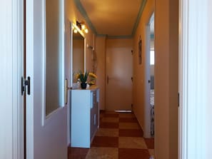 Ein Korridor mit einem Schachbrettmuster auf dem Boden, einem weißen Schrank mit Pflanze und einer Tür am Ende.