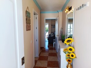 A hallway with a checkered floor, a door on the left, and a mirror on the right with sunflowers. - Renovated Apartment with Sea-View Terrace and Pool in Los Álamos, Torremolinos (Torremolinos)