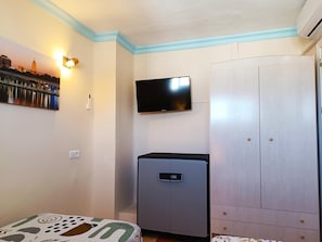 Ein Zimmer mit einem Bett, einem Kleiderschrank, einem an der Wand befestigten Fernseher und einer Wandleuchte.