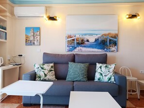Ein Wohnzimmer mit einem grauen Sofa, zwei weißen Beistelltischen und einem großen Gemälde von einer Strandansicht.