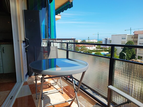 Ein Balkon mit Glastisch und Metallgeländern, der auf ein Wohngebiet mit Gebäuden und einem klaren Himmel blickt.