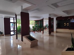 Een ruime lobby met een receptiebalie, plantenbakken en een groot open gebied.