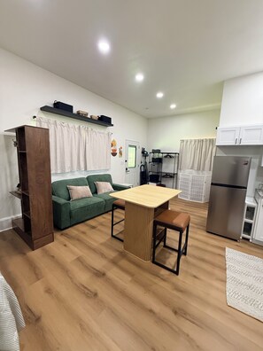 A compact living space with a kitchenette, a dining area with a wooden table, a green sofa, and a brown cabinet. - The R&R Studio  Cozy Private Guesthouse (Fayetteville)