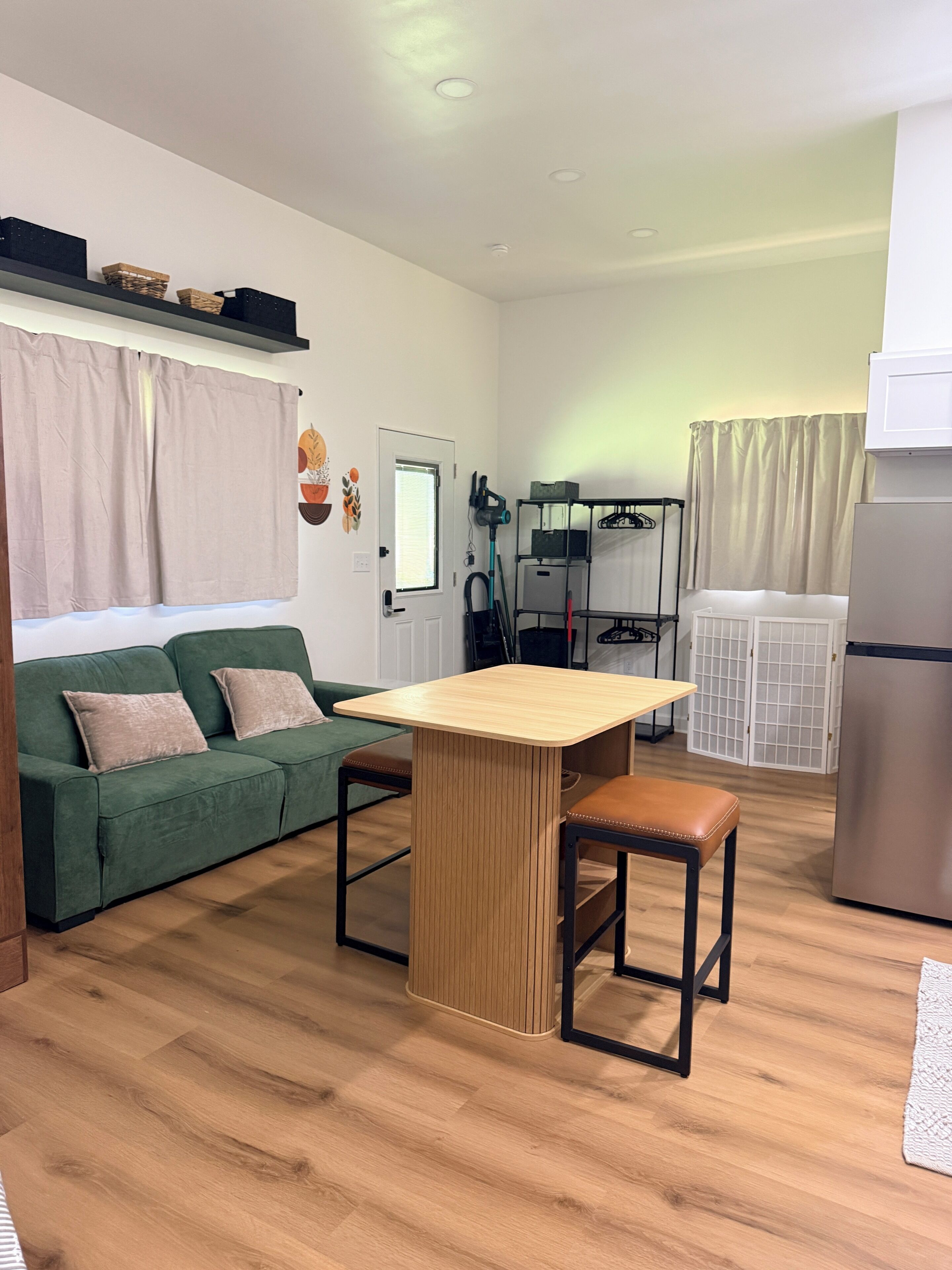 Een compacte woonruimte met een kitchenette, een groene bank, een houten eettafel en een witte koelkast.