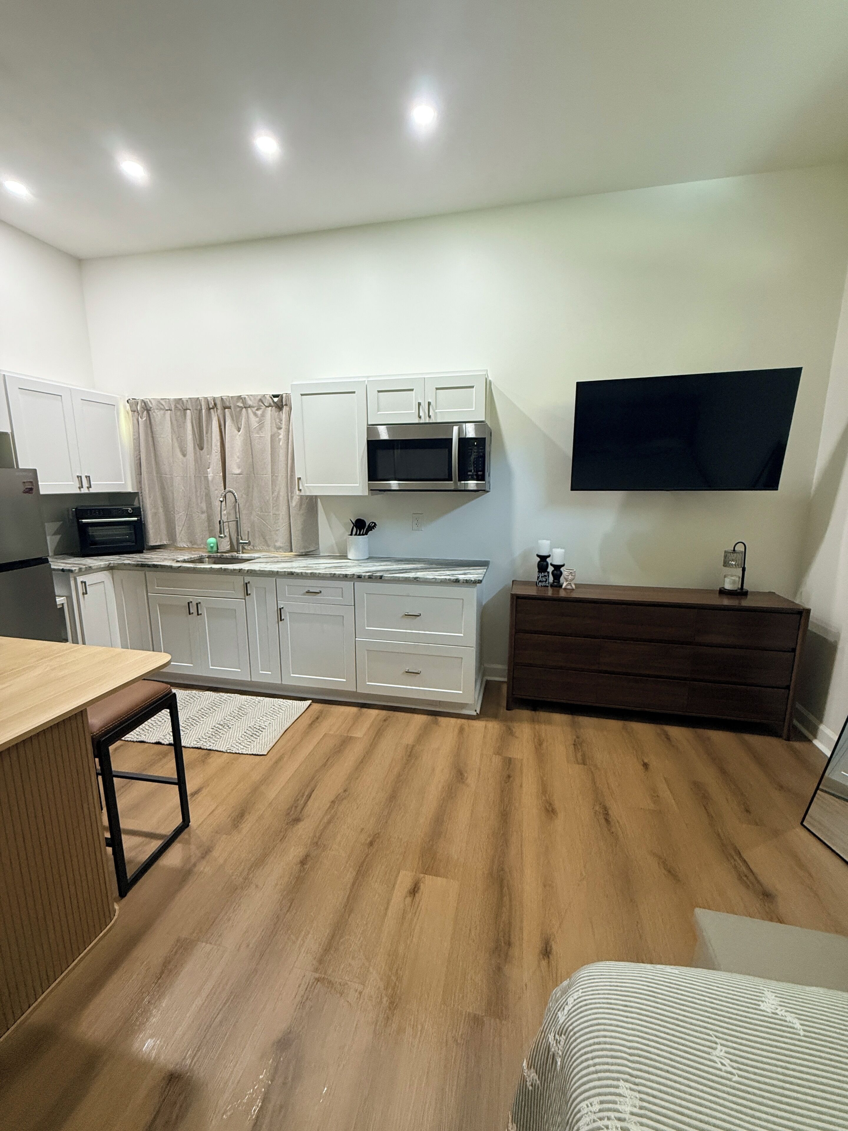 A modern kitchen with white cabinetry, a built-in microwave, and a flat-screen TV mounted on the wall.
