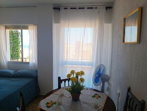 A room with a bed, a table with a plant, a fan, and a window with curtains. - Renovated Studio with Sea-View Terrace and Pool in Central Torremolinos (Torremolinos)